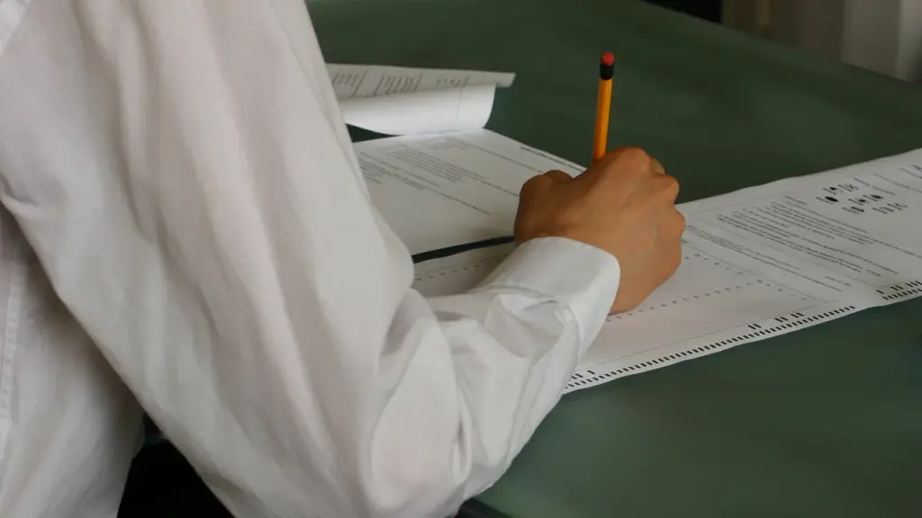 Pessoa escrevendo respostas em uma avaliação sobre a mesa da sala de aula