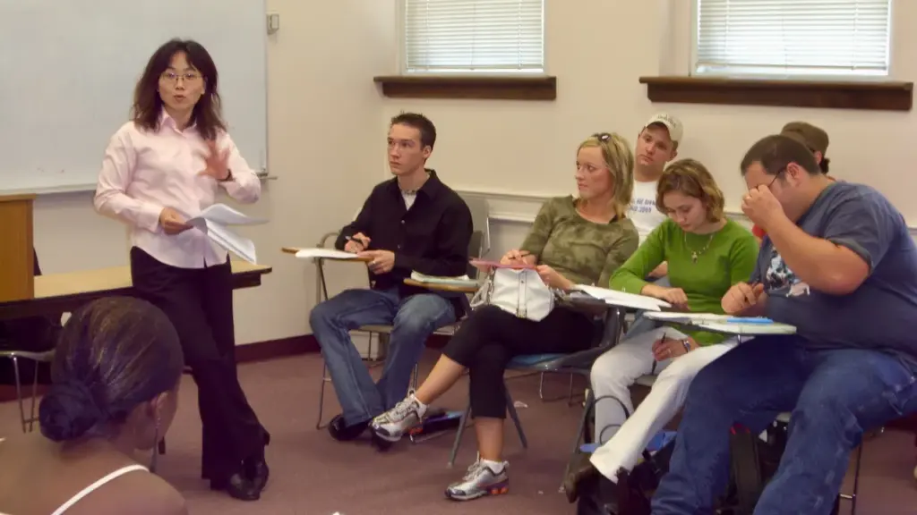 Professora orienta uma discussão enquanto estudantes trabalham em uma sala de aula.