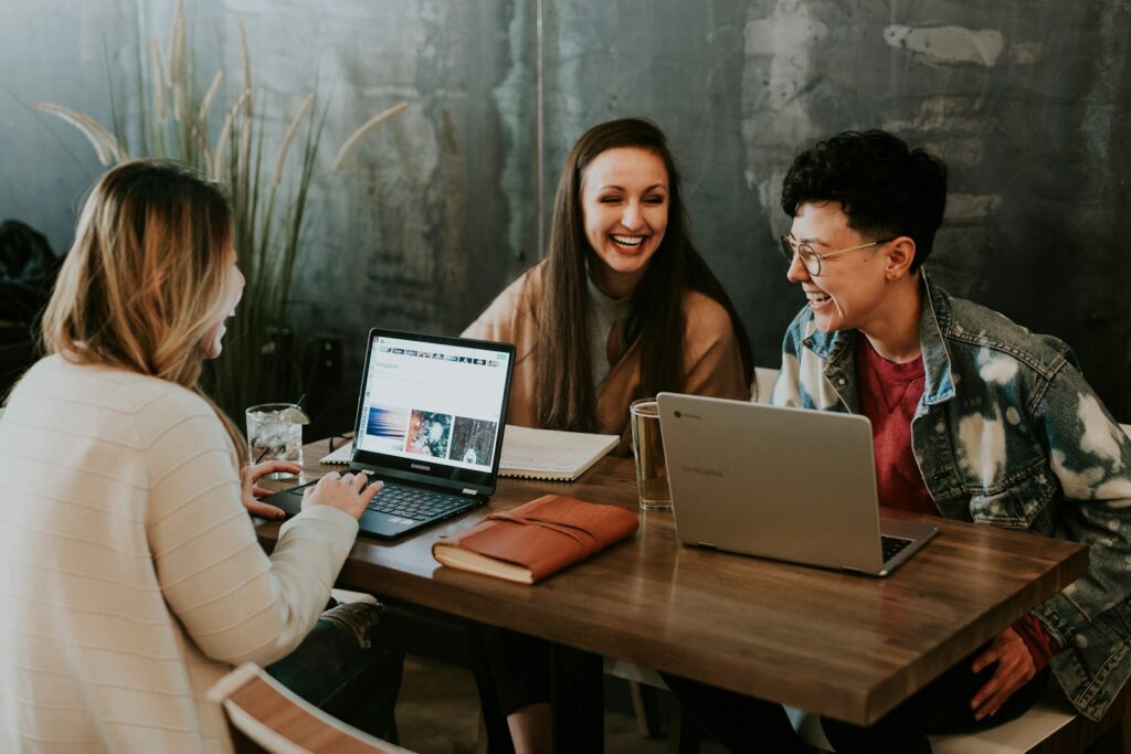 Três estudantes colaboram com dois laptops em uma mesa; fonte e crédito: Unsplash, foto 1522202176988-66273c2fd55f.