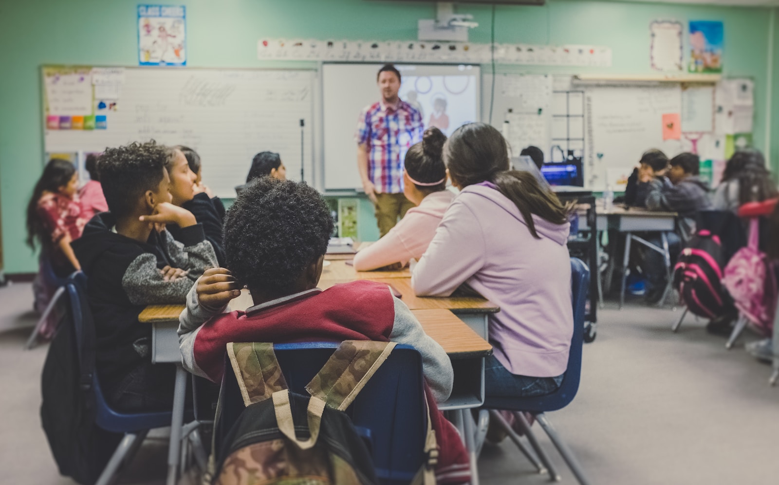 Professor conduz aula enquanto estudantes acompanham em uma sala de aula; fonte e crédito: Unsplash, foto 1509062522246-3755977927d7.