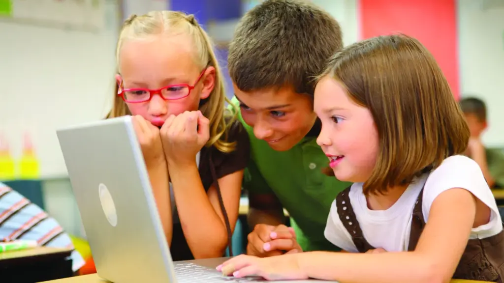 Três estudantes analisam juntos uma atividade em um computador na sala de aula