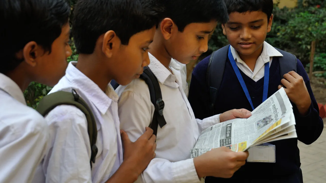 Estudantes leem juntos um jornal impresso em uma atividade de leitura e produção de mídia