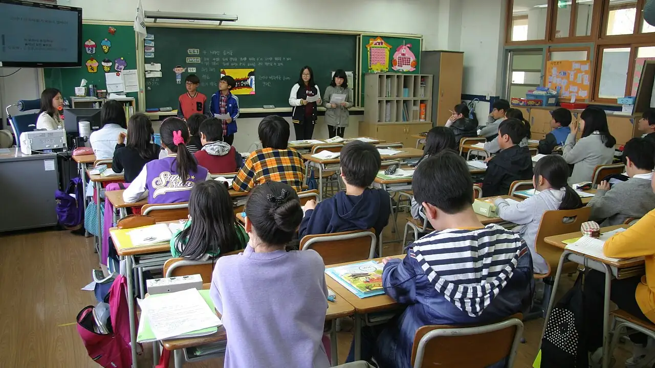 Turma de estudantes em sala de aula acompanha uma apresentação e analisa materiais