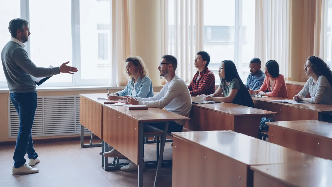 Professor orienta uma turma sentada em mesas, em uma sala de aula.
