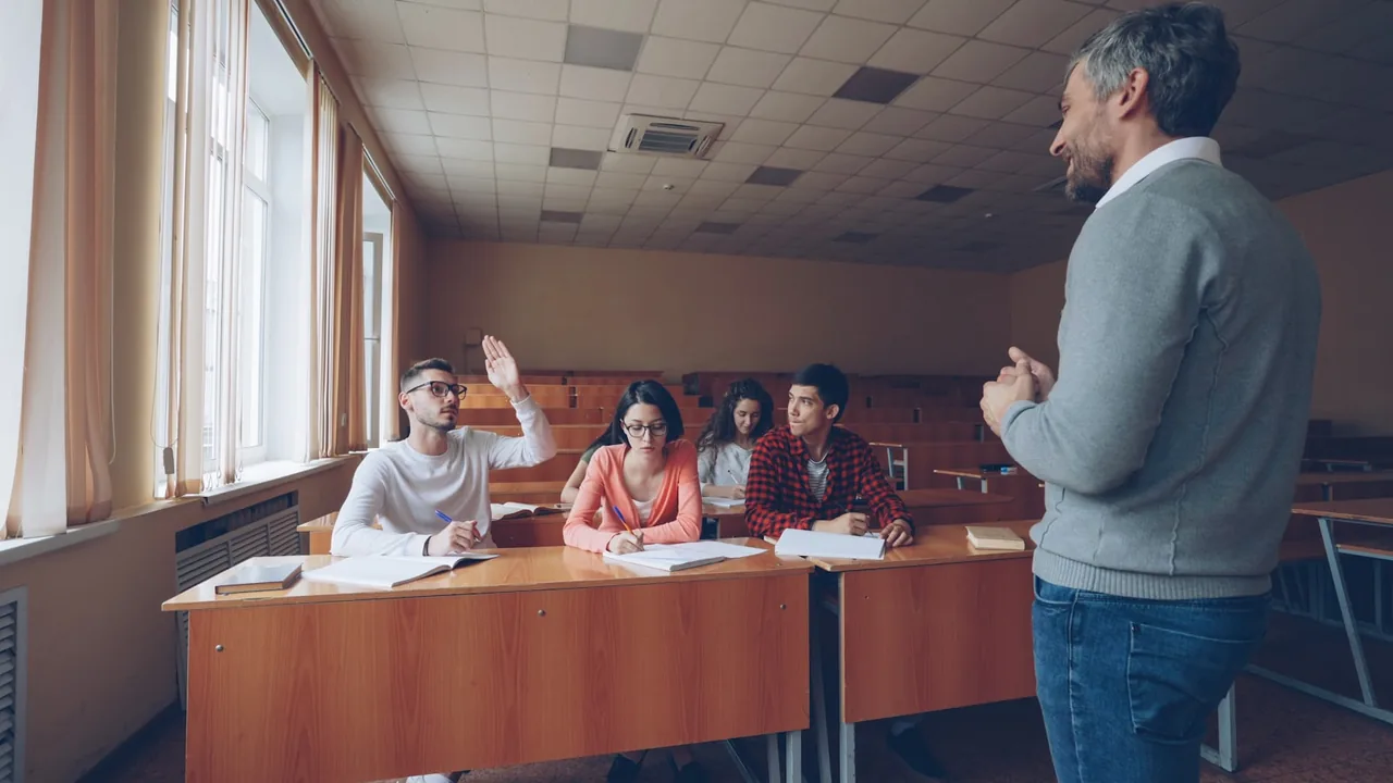 Professor conversa com estudantes em uma sala de aula durante uma atividade.